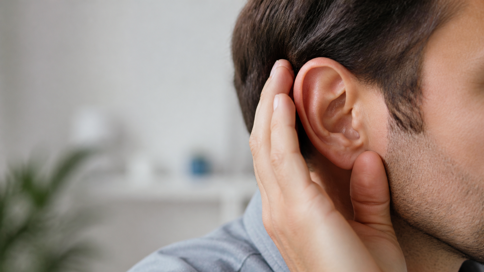 Close-up of a person holding their hand behind their ear as if trying to hear better.